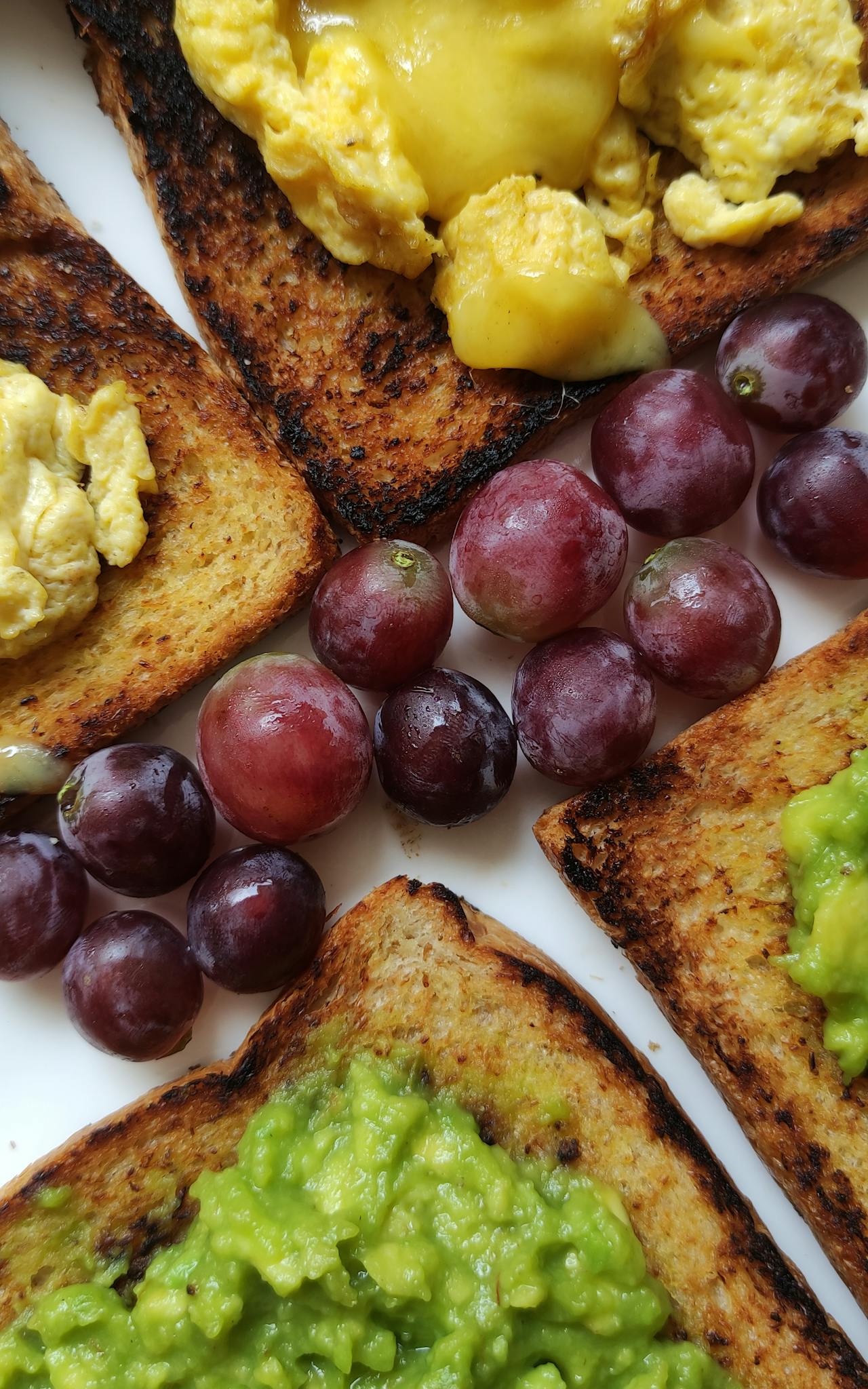 A vibrant breakfast plate featuring avocado toast, grapes, and scrambled eggs.