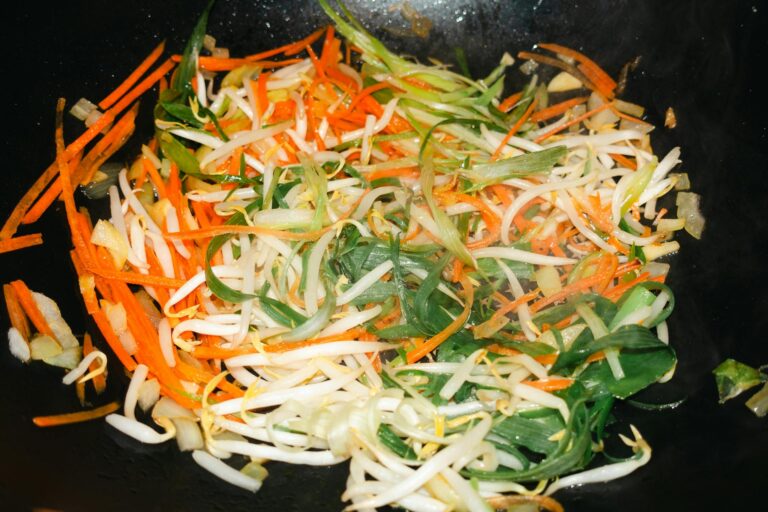 A vibrant mix of vegetables stir-fried in a wok, featuring carrots and bean sprouts.